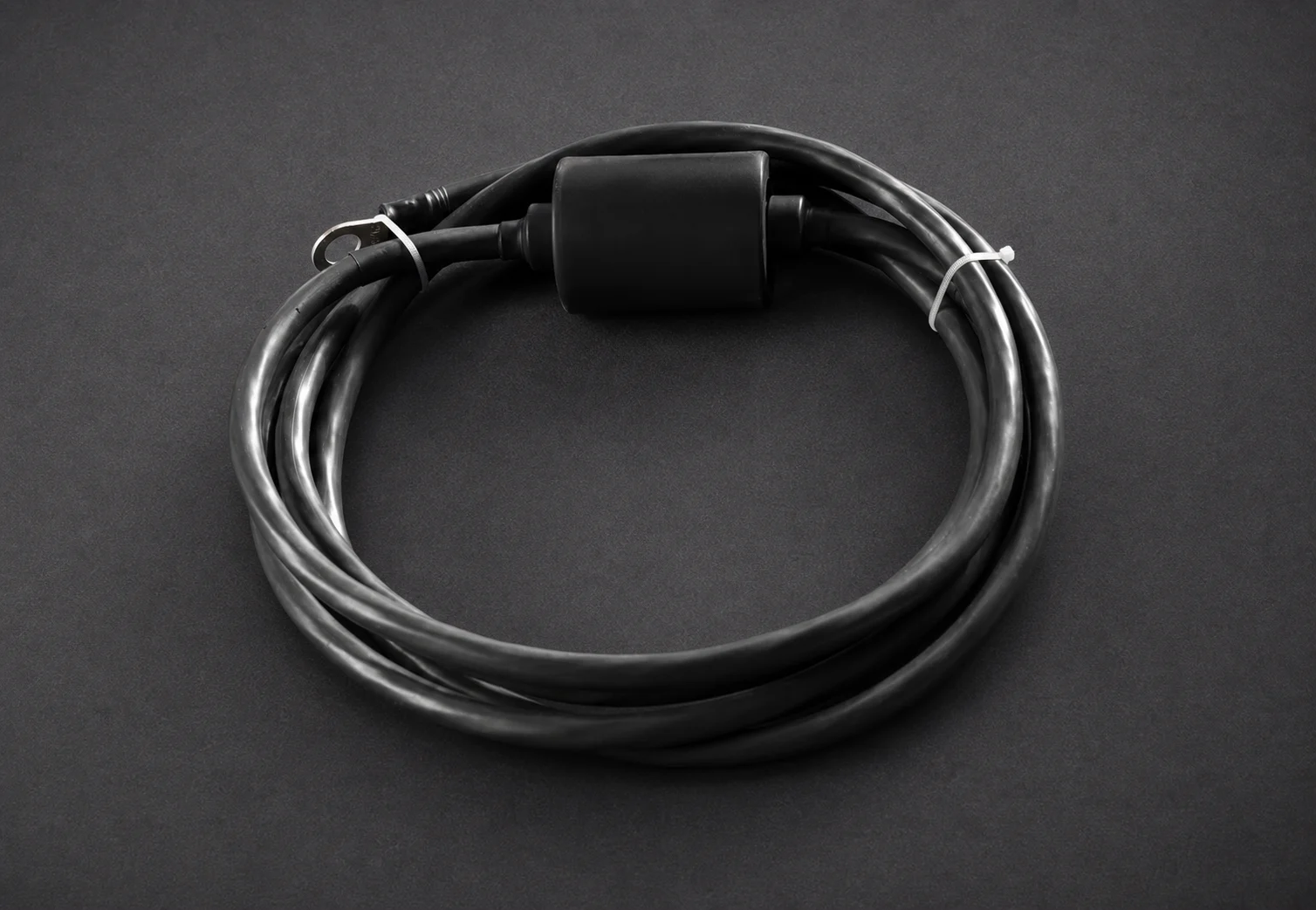 Coiled black cable assembly with a sealed connection body on a studio background